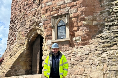 Man stood in front of the castle in a yellow high vis jacket and a hard hat